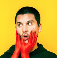 a man with red gloves covering his face on a yellow background